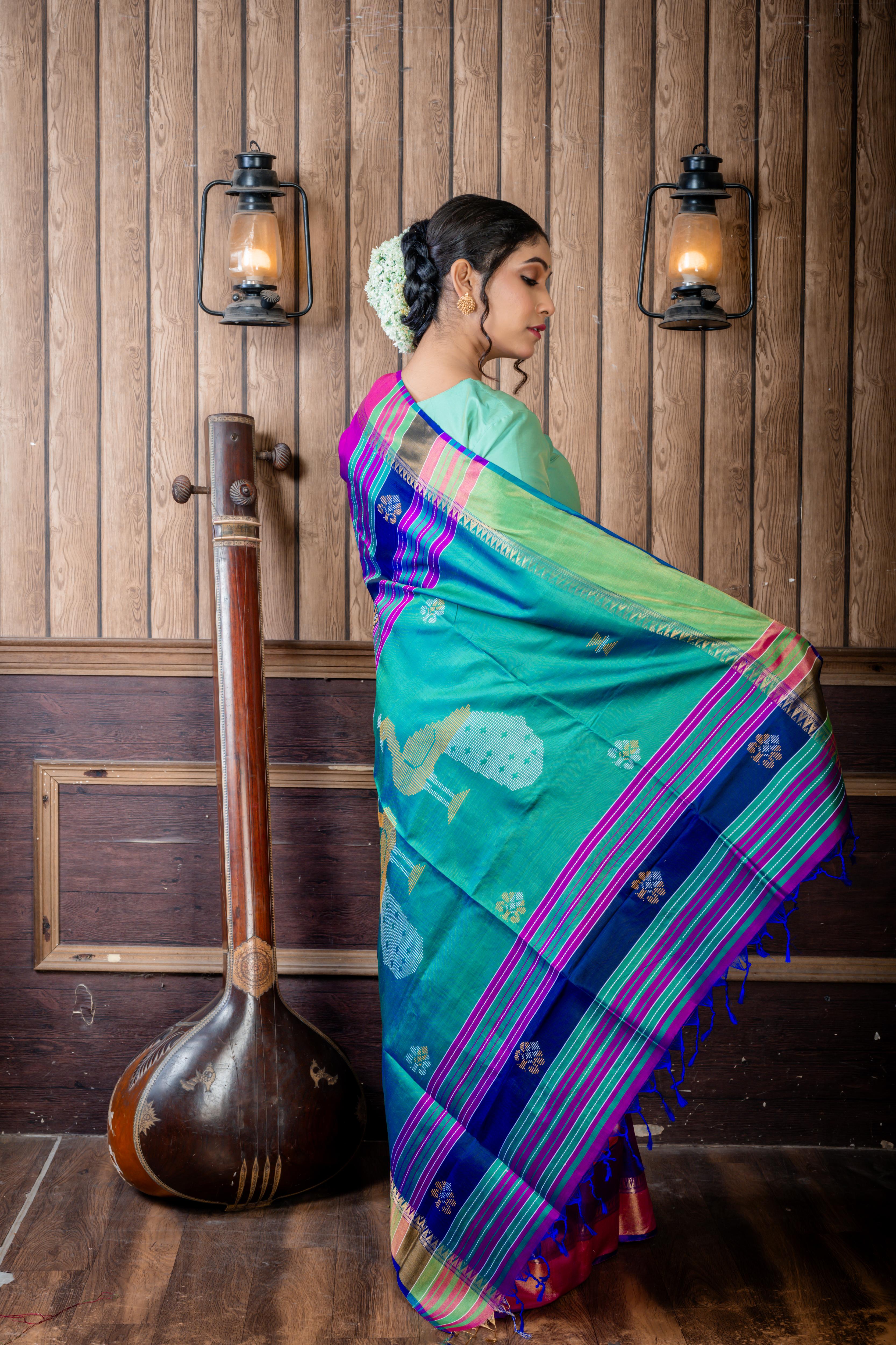 Pritha || Purple & Royal Blue dual tone Pure Bishnupuri Katan Handloom 'Kalakshetra' Embroidery Saree with all over Multi-colour Floral Buta and Stripe & 'Peacock' motif Green Pallu